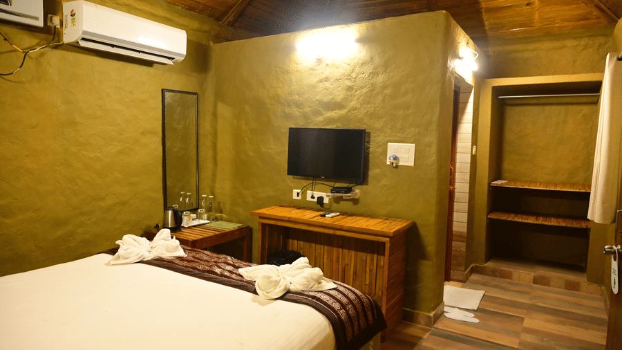 A wider view of a room interior at Pipul Odi Art Museum Resort, showing the double bed, a wooden dressing table area with a mirror, a television, and the warm-toned lighting.