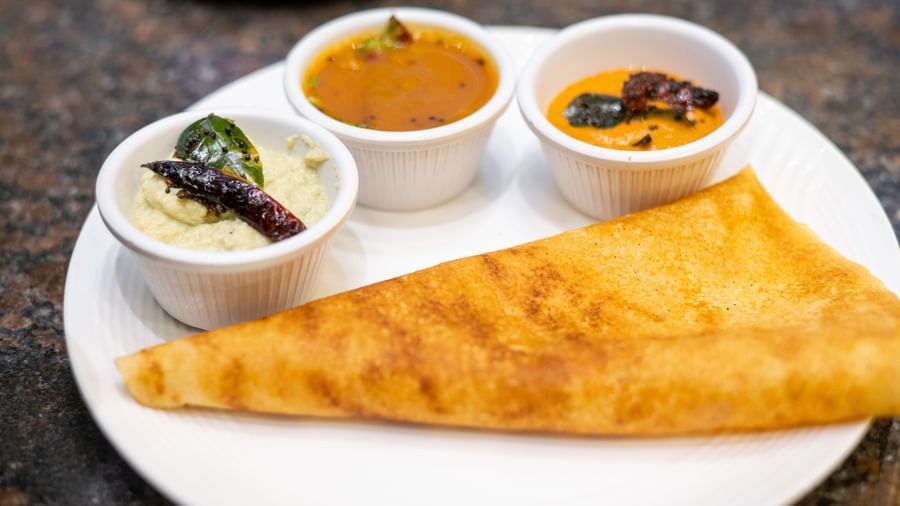 A golden rolled dosa is served with three small bowls of sambar and chutney at Pravasa Stay, Shirdi.