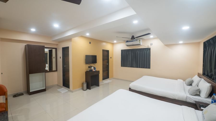 A spacious room at Pravasa Stay, Shirdi, contains two beds, a wardrobe, and a television on a small desk.
