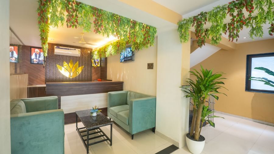The reception area of Pravasa Stay, Shirdi, has two cushioned chairs and a desk adorned with a gold emblem.