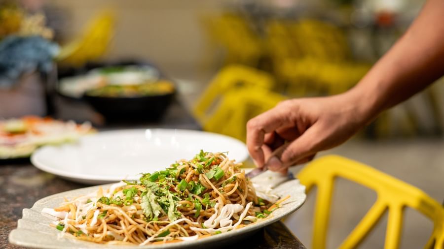 A waiter is adjusting the garnish on a plate of noodle dish at the restaurant of Pravasa Stay, Shirdi.