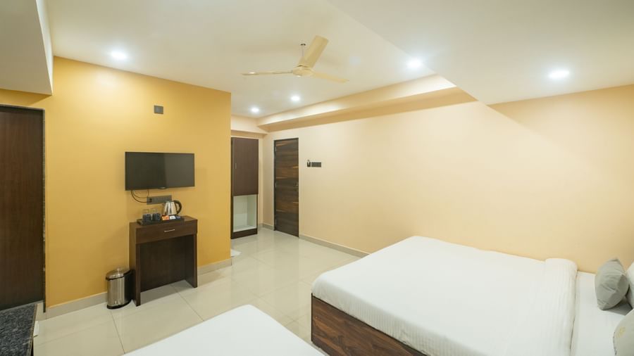 A room at Pravasa Stay, Shirdi, has two beds, a wall-mounted television, and a desk in the corner.