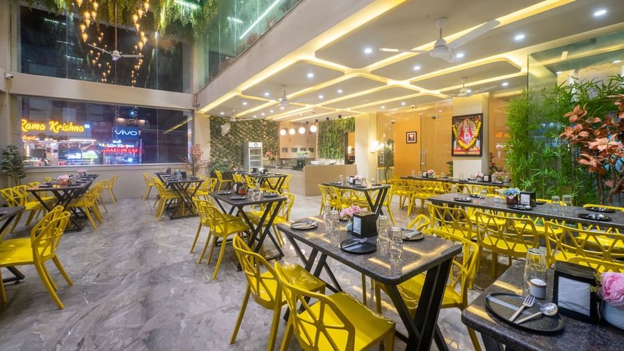 The dining space at Pravasa Stay, Shirdi, features bright yellow chairs and many ceiling lights.