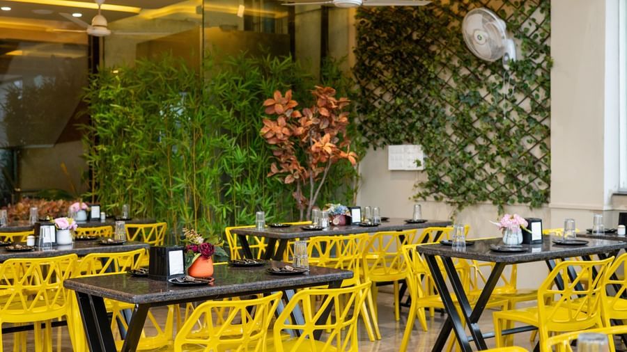 The seating area of the Pravasa Stay, Shirdi restaurant is filled with bright yellow chairs and black tables.