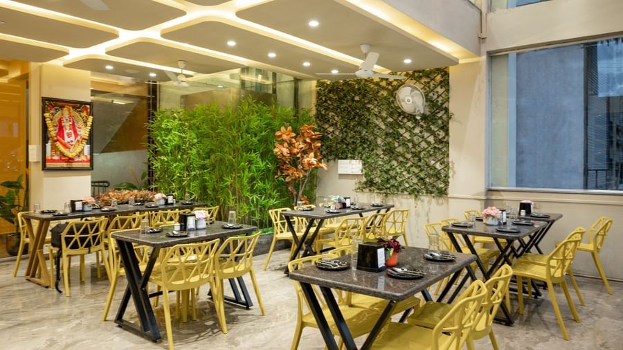 The restaurant at Pravasa Stay, Shirdi, has yellow chairs, black tables, and decorative green walls.