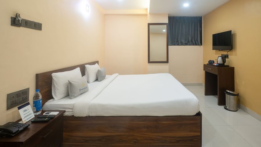 This room at Pravasa Stay, Shirdi, features a large wooden bed frame, a mirror, and a television on the opposite wall.