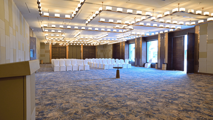 A large, empty event hall with a patterned carpet, modern lighting, and chairs set up for a gathering | Pushkara Resort & Spa, Ajmer