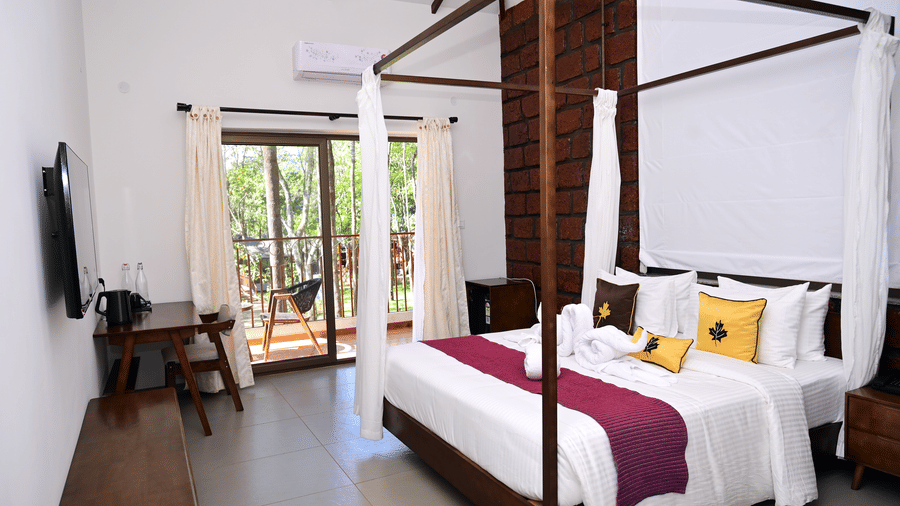 A Premium Cottage at TGI Redolent Resort, Kushalnagar, Coorg, featuring a bedroom with a poster bed, a flat-screen TV, a work desk and chair, and a balcony.