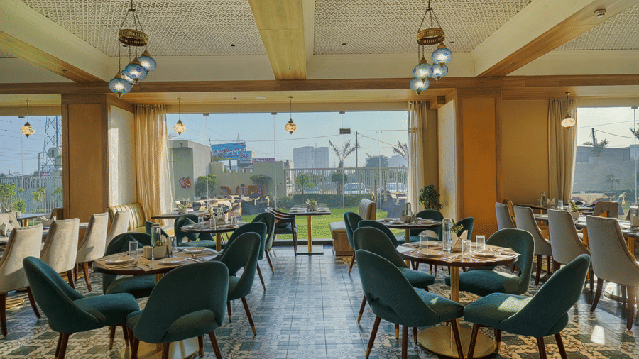 A dining space in Urban Rasoi at Urban Suites by BluSalzz, Jaipur, with tables and chairs, offering panoramic city views through large windows.