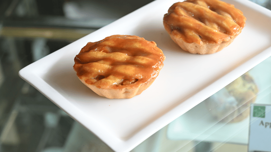 Two golden baked pastries with a lattice pattern served on a white platter at Vedic Village Spa Resort Kolkata displayed in a glass showcase counter.