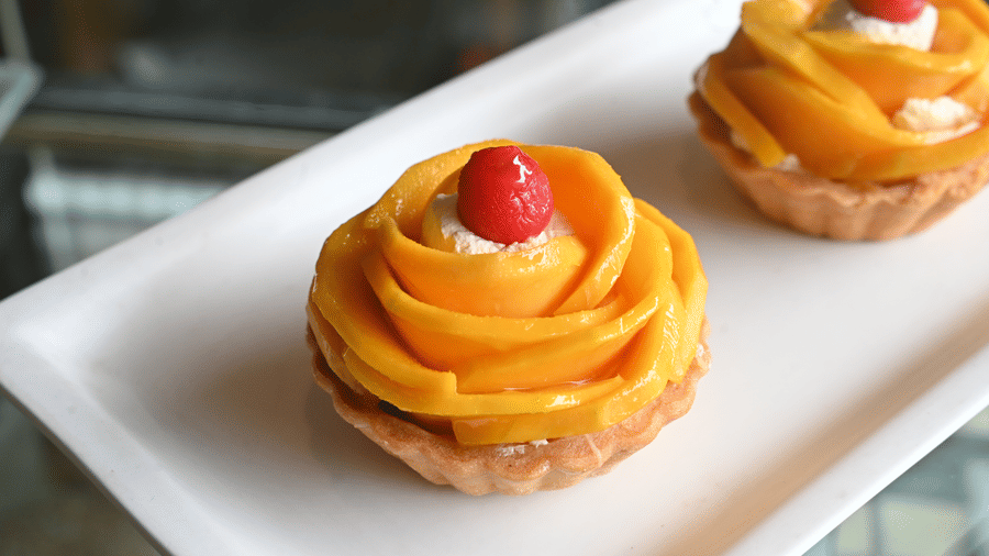 A white platter featuring two fruit tarts topped with mango slices and a strawberry served at Vedic Village Spa Resort Kolkata in a close-up food presentation.