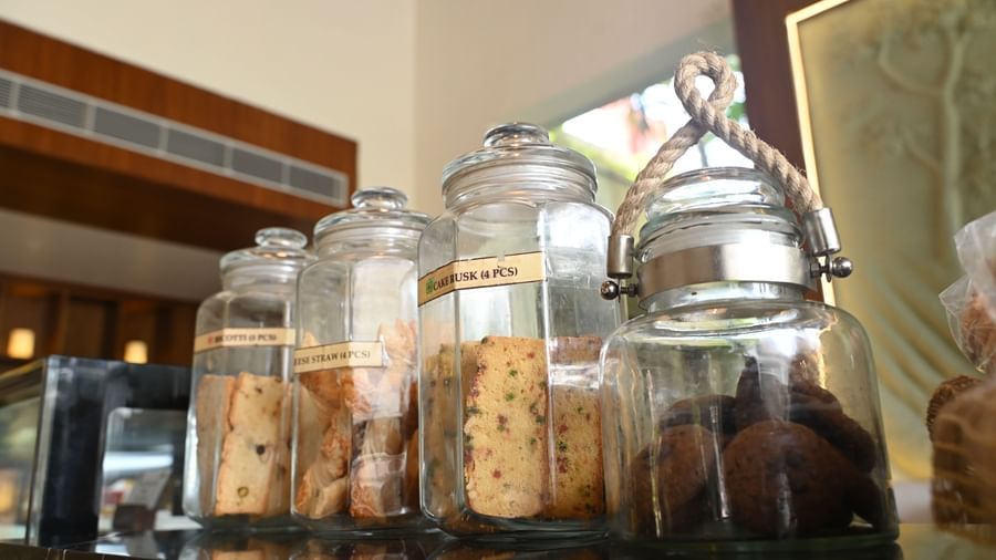 Several clear glass jars filled with various types of cookies are displayed on a shelf in a cafe setting | Vedic Village Spa Resort, Kolkata