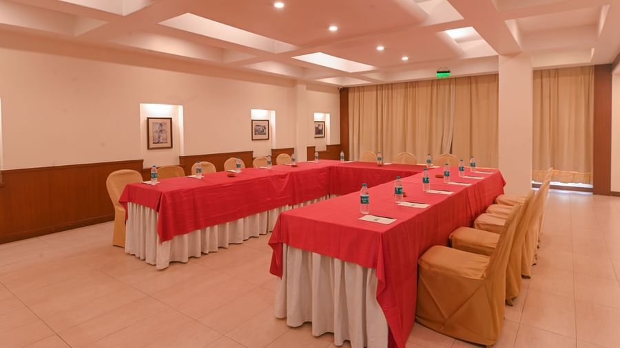 A well-lit conference hall in Vedic Village Spa Resort featuring modern interiors and chairs arranged to one side of two tables.