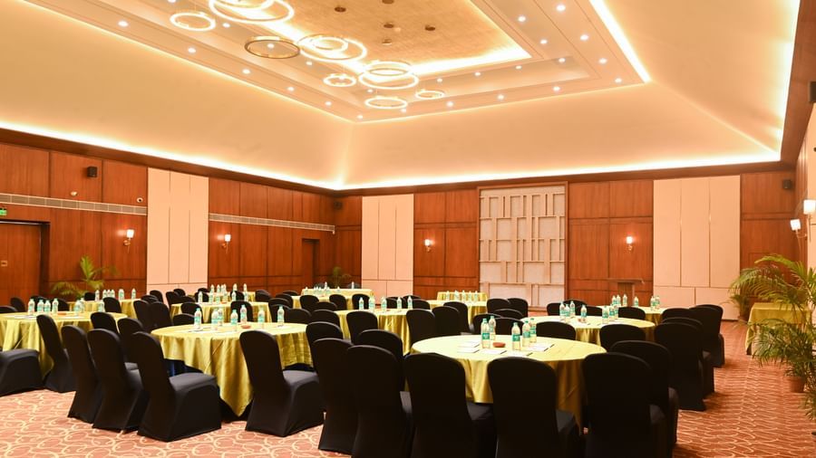 Om ballroom in Vedic Village Spa Resort, featuring a spacious hall with circular tables, black chairs, and well designed ceilings.