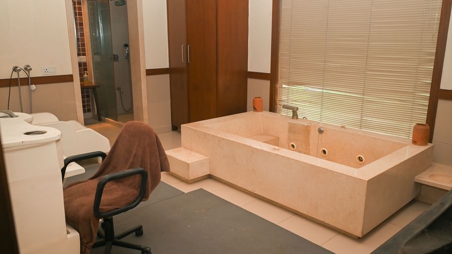 Spa therapy room in Vedic Village Spa Resort, featuring a bathtub and private shower area.