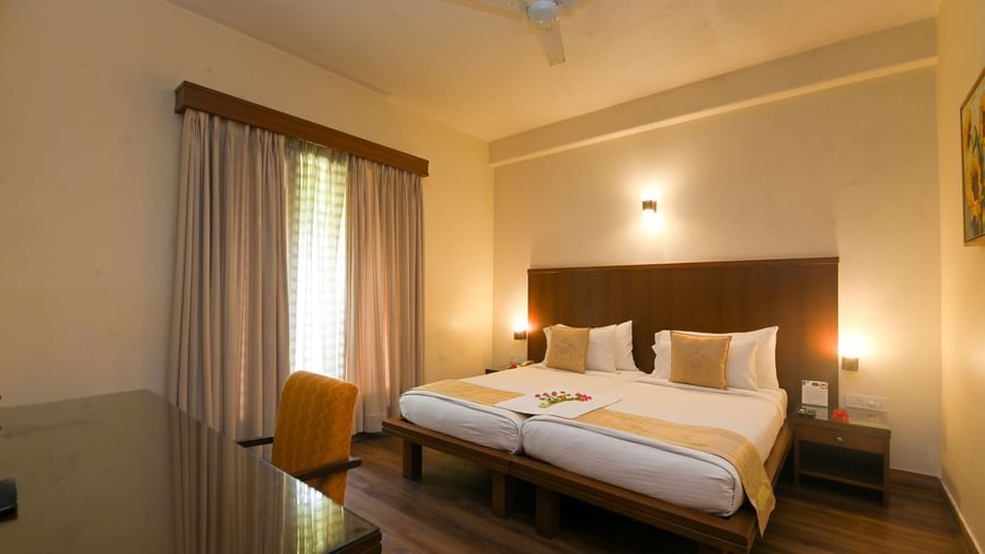 Warmly lit Superior Room at Vedic Village Spa Resort showcasing a double bed, wooden flooring, ceiling fan, and a work desk with chair for added convenience.