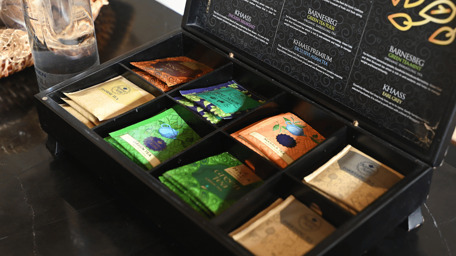 A black gift box with assorted tea sachets and premium packaging on display at Vedic Village Spa Resort Kolkata with gold embossed detailing on the box lid.