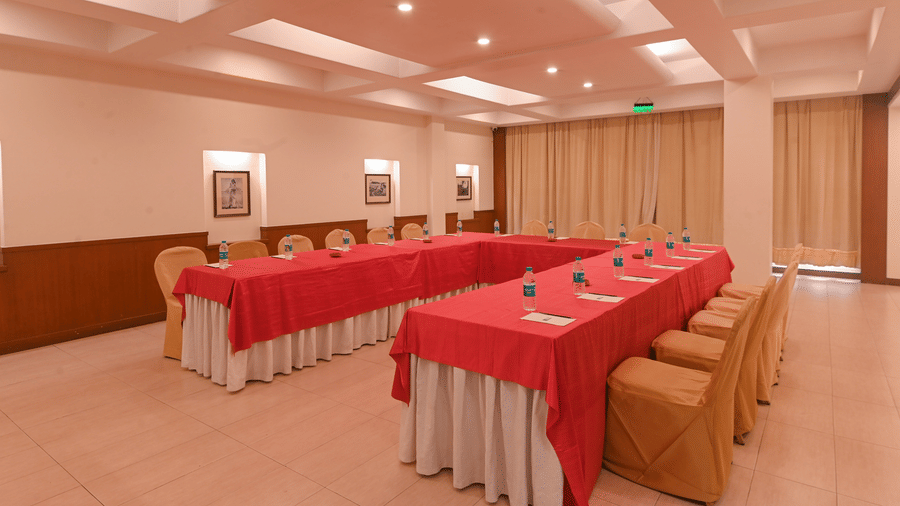 Conference room at Vedic Village Spa Resort Kolkata arranged in a U-shape with red table linen, chairs, framed artwork on the wall, and warm ambient lighting.
