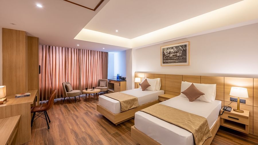 Close up shot of Twin Room at Vishranti Hotel, Dehradun featuring twin beds, side table with bed lamp and a work desk.