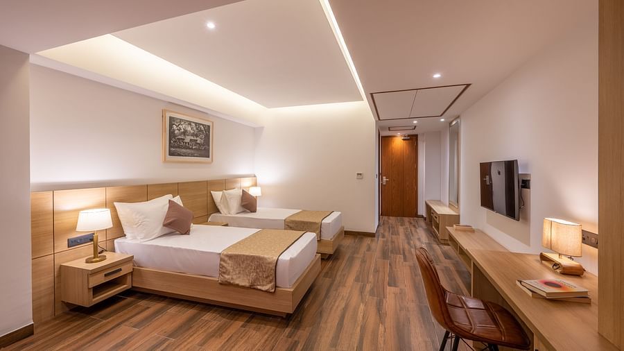 Side shot of Twin Room at Vishranti Hotel, Dehradun featuring twin beds, side table with bed lamp and a work desk.
