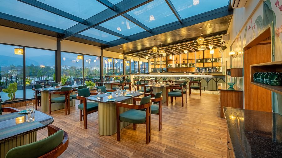 Overview of  interiors of The Gaia Gourmet restaurant at Vishranti Hotel, Dehradun, featuring a well-lit dining area with glass rooftop, wooden floors.