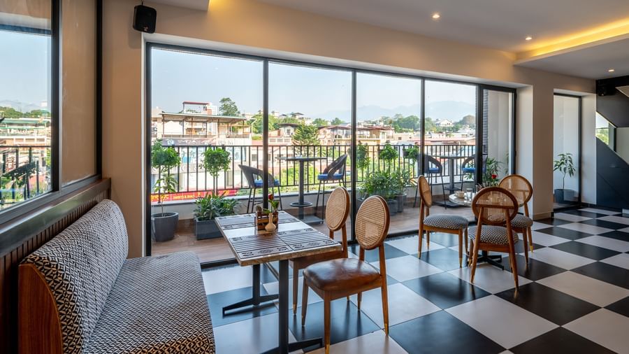 Side shot of a bar at Vishranti Resort Dehradun with chairs, sofas, tables, a counter and checkered floors. 