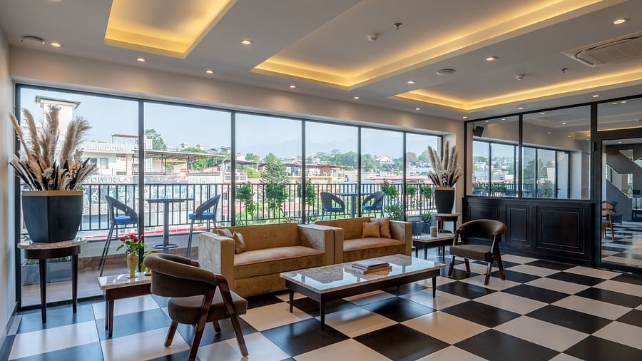 Shot of a bar at Vishranti Resort Dehradun with chairs, sofas, tables, a counter and checkered floors. 