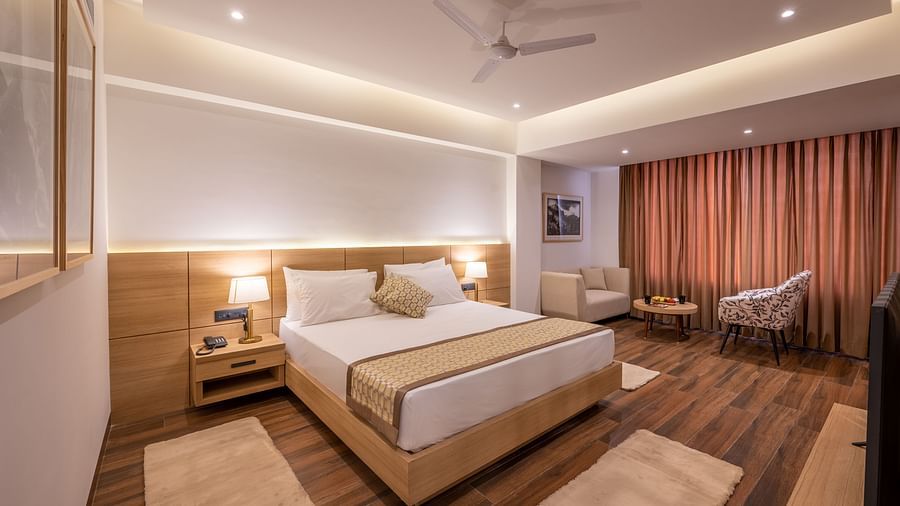 Overview shot of Premium Room at Vishranti Hotel, Dehradun featuring a king bed with side tables, a TV, large window and bed lamps. 