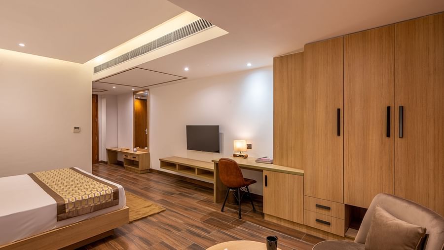 Close up shot of Suite at Vishranti Hotel, Dehradun featuring a king bed with side tables, a TV, large window with curtains and bed lamps. 
