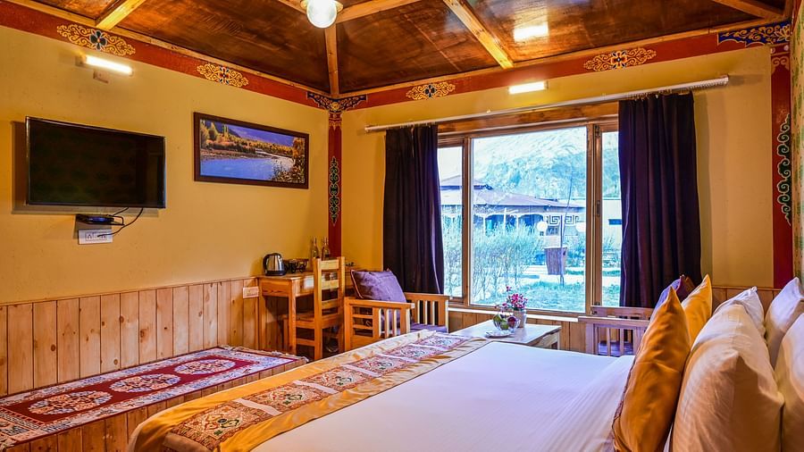 Premium Cottage at White Sands Resort, Ladakh features a king size bed with patterned linens, a seating area, and a view of the outdoors through a window.