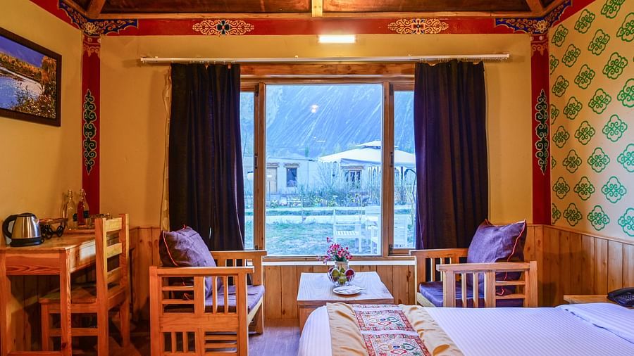Premium Cottage at White Sands Resort, Ladakh, is furnished with a king size bed, a dining table, chairs, and vibrant wallpaper.