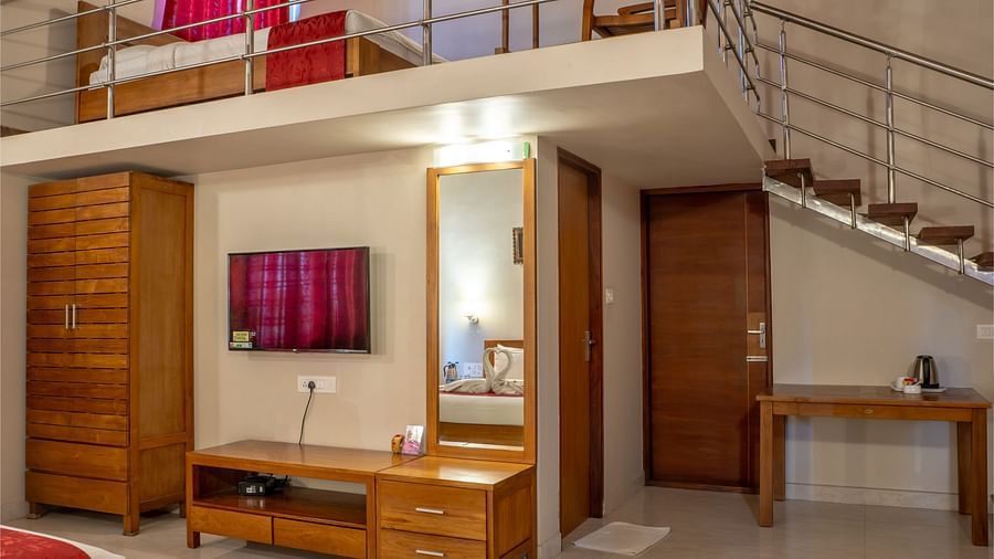 Attic Villa features a staircase leading to a loft area with a bed, along with a desk and television | Woodstock Resorts, Coorg