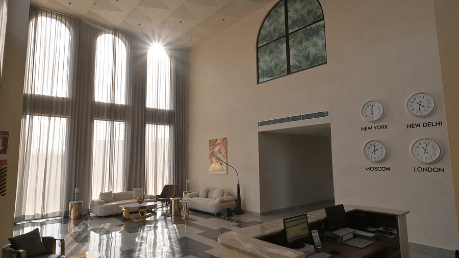 A high-ceilinged lobby area features large windows, seating, and wall-mounted clocks displaying different time zones. - Clarks Safari Haridwar