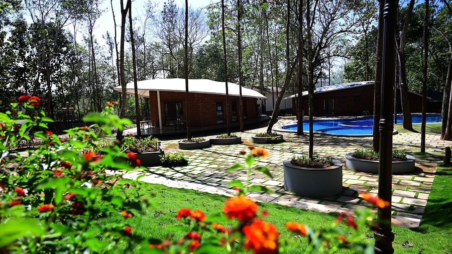 An outdoor area of TGI Redolent Resort, Kuslanagar, featuring a garden, hut style cotttages, a swimming pool, and much more