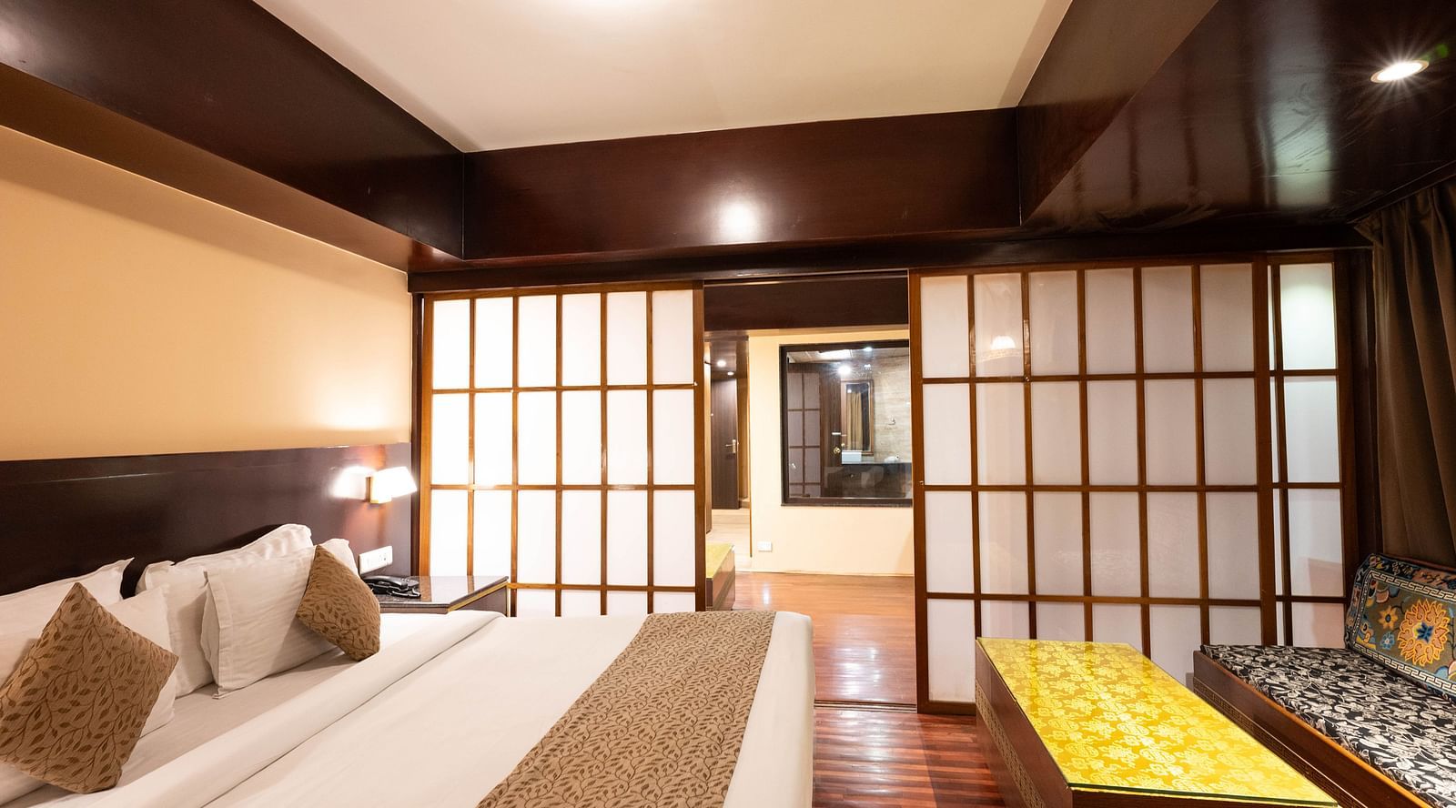 A bedroom with a large bed, sliding doors, and a cushioned seating area near a table at Avianna Hungry Jack, Gangtok.
