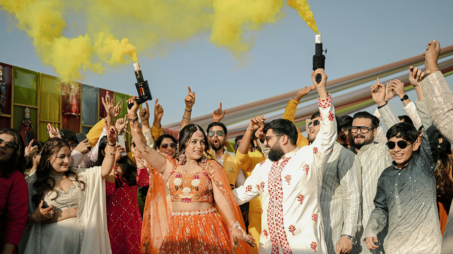 Bride and groom celebrating the haldi ceremony with colour popper with their friends and family.