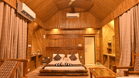 Bamboo cottage bedroom with a bed dressed in patterned linen, a wooden ceiling fan, long curtains and warm wooden panelled walls throughout.