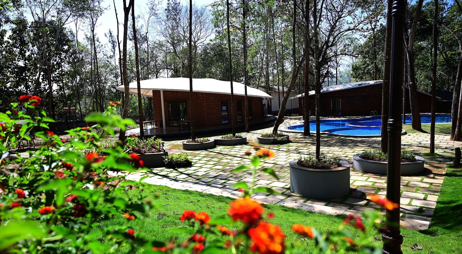 An outdoor area of TGI Redolent Resort, Kuslanagar, featuring a garden, hut style cotttages, a swimming pool, and much more
