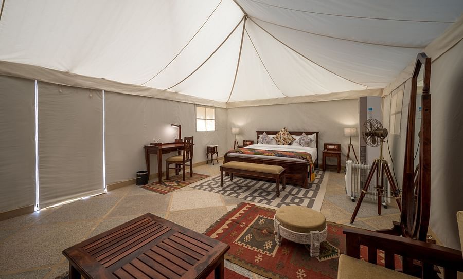 alt-text The interiors of the Premium Camp offers a spacious bed, a mirror, a teapoy and other amenities - Karwaan Jaisalmer