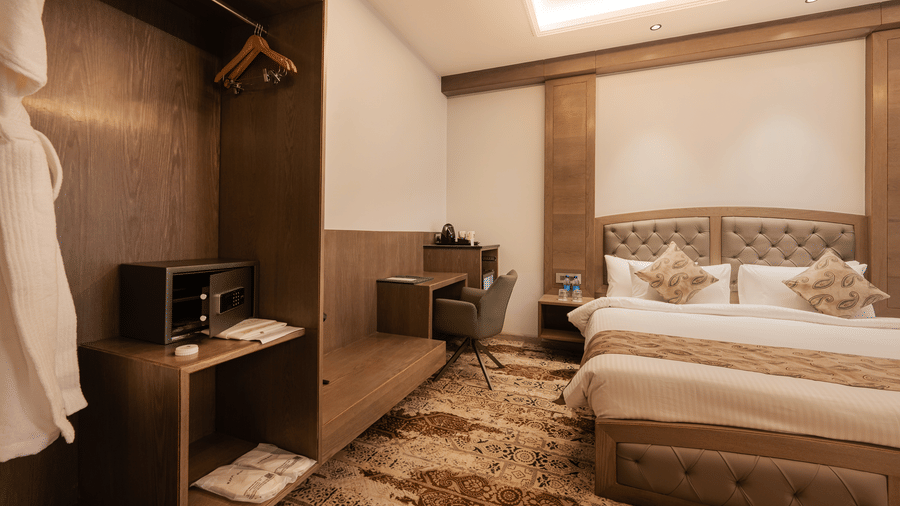 A bedroom interior showing a wooden wardrobe, a small work desk with a chair, and a king-sized bed at Ananta Express, Katra.