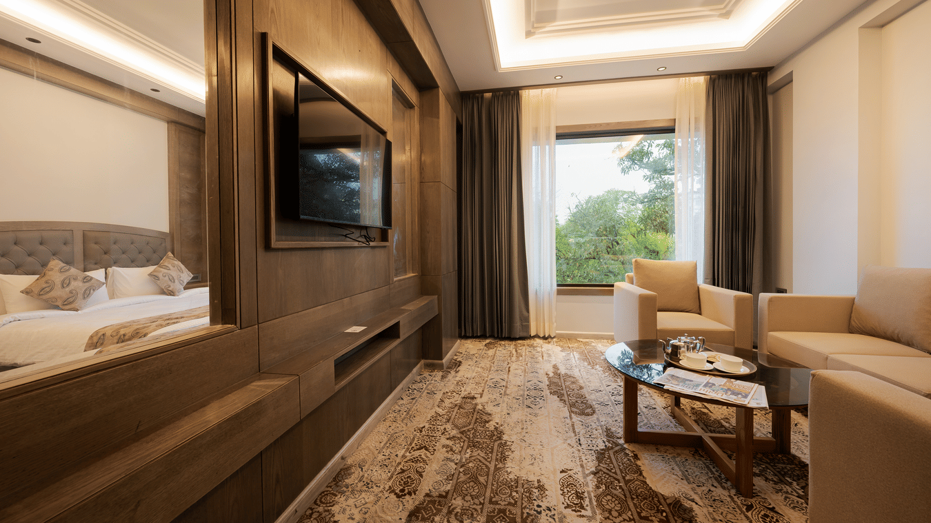 A modern guest suite featuring a king-sized bed, a wall-mounted television, and a window with a green landscape view at Ananta Express, Katra.