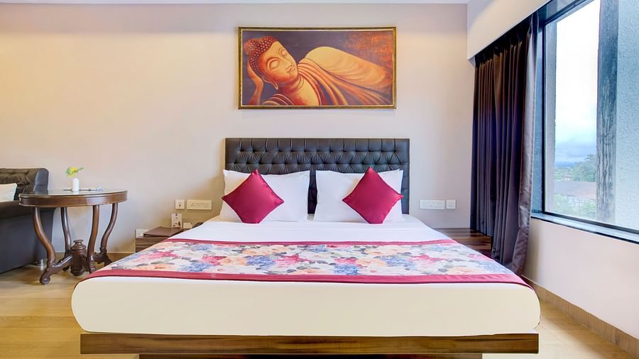 Elegant bedroom featuring a vibrant bedspread, wall art, and a large window with city views at Voyage Milestone Hotel and Banquet Siliguri