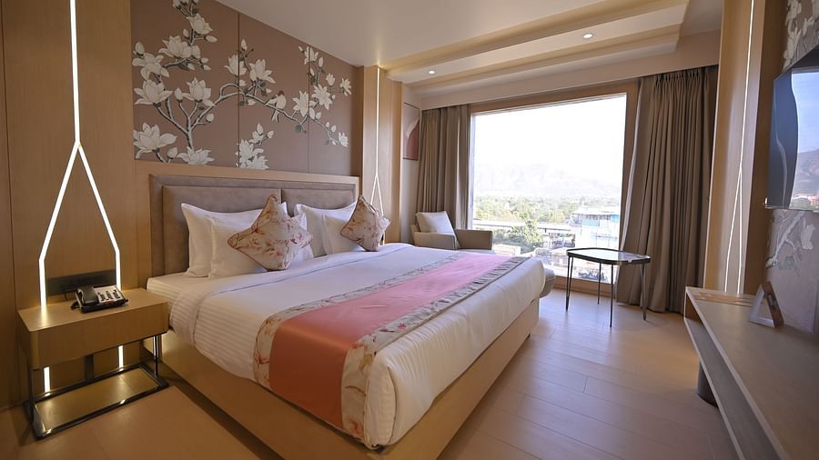 A bedroom featuring a flower painting above the bed and large windows with open curtains allowing natural light to fill the space at Clarks Collection Grand Sapphire, Ajmer.