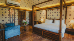 A Premium Duplex Tent bedroom featuring a sofa, a poster bed, bedside table with lamps on either side, cabinet table, a wardrobe, and a centre table with flower vase at The Baagh Ananta Elite, Ranthambore