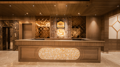 A large wooden and marble reception desk illuminated by warm lighting in the main lobby at Ananta Express, Katra.
