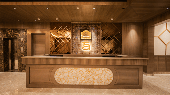 A large wooden and marble reception desk illuminated by warm lighting in the main lobby at Ananta Express, Katra.