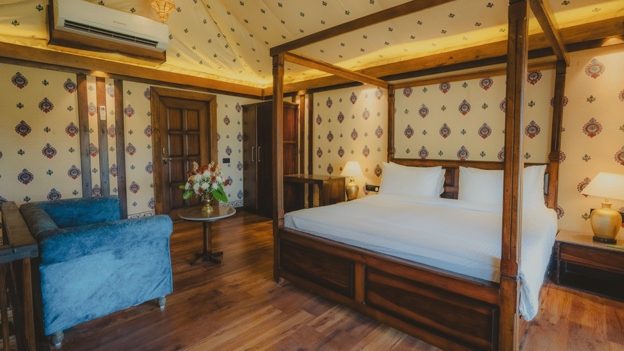 A Premium Duplex Tent bedroom featuring a sofa, a poster bed, bedside table with lamps on either side, cabinet table, a wardrobe, and a centre table with flower vase at The Baagh Ananta Elite, Ranthambore