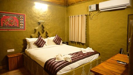 The interior of a room at Pipul Odi Art Museum Resort, showing a double bed, green walls, a split-unit air conditioner, and a wooden ceiling.