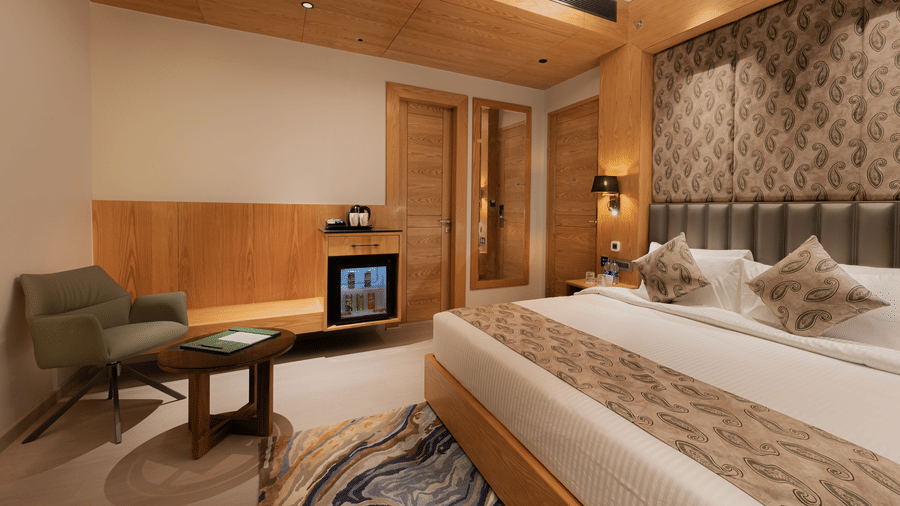 A guest room featuring a king-sized bed, a green armchair, and a wooden cabinet with a minibar at Ananta Express, Katra.