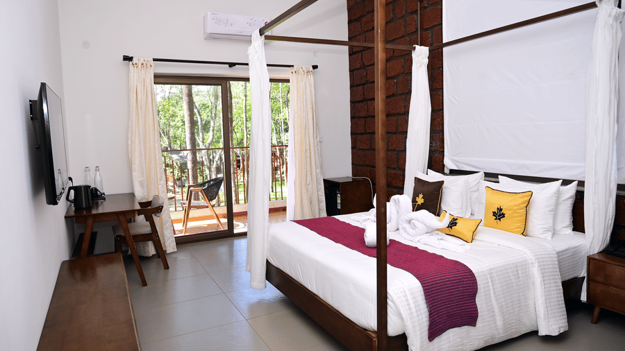 A Premium Cottage at TGI Redolent Resort, Kushalnagar, Coorg, featuring a bedroom with a poster bed, a flat-screen TV, a work desk and chair, and a balcony.